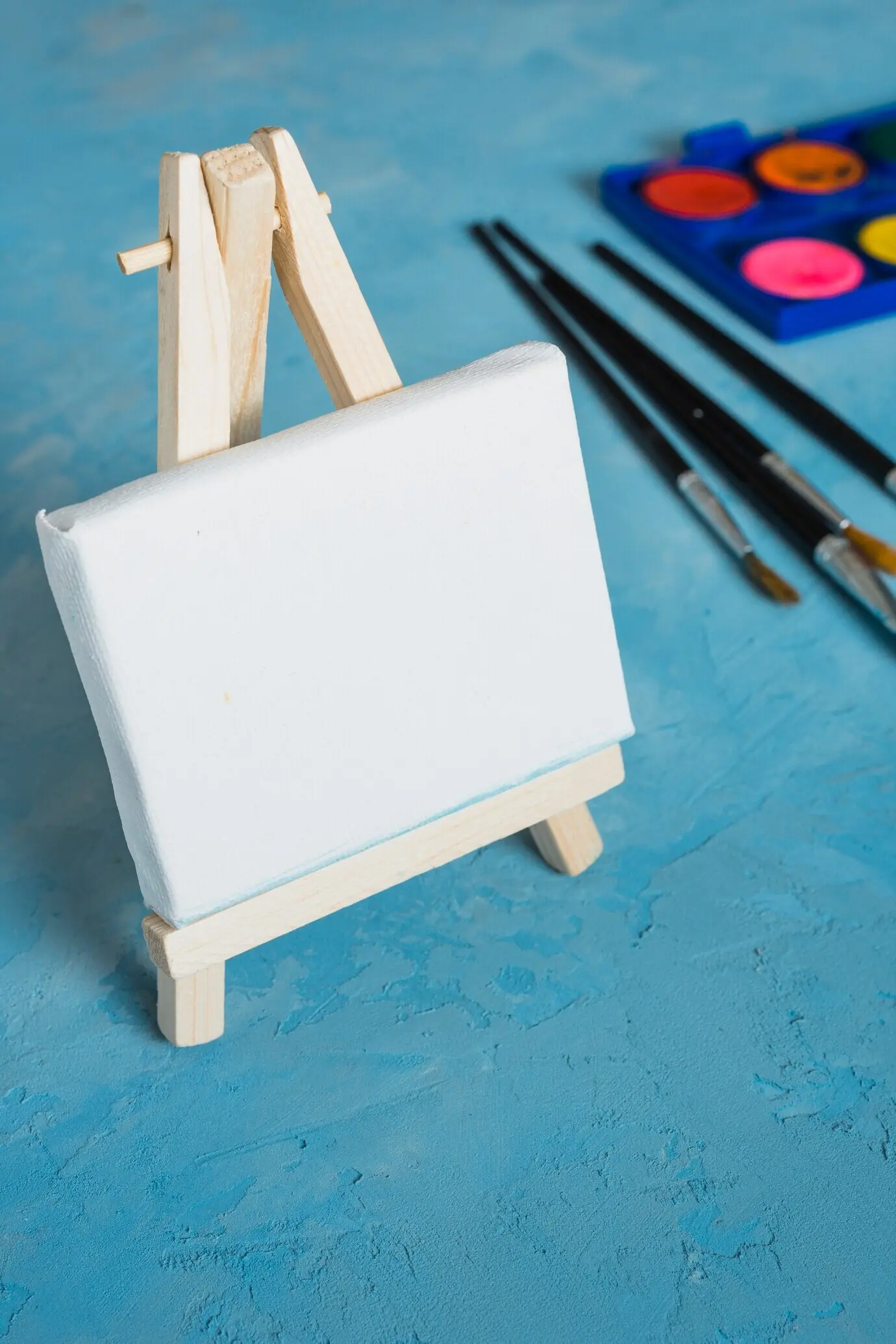 Kleine weiße leere Holzstaffelei mit Pinsel auf blauem texturierten Hintergrund.